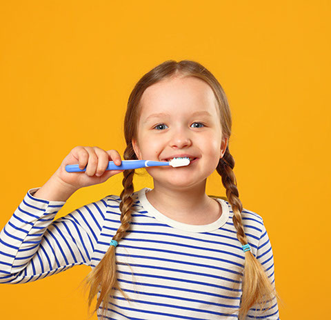 girl in pigtails smiling while brushing her teeth