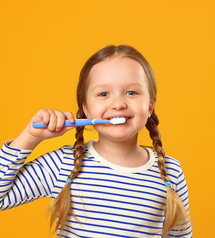 girl in pigtails smiling while brushing her teeth