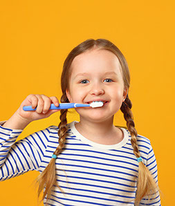 girl in pigtails smiling while brushing her teeth