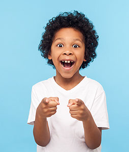 boy with a huge smile and curly hair pointing straight ahead